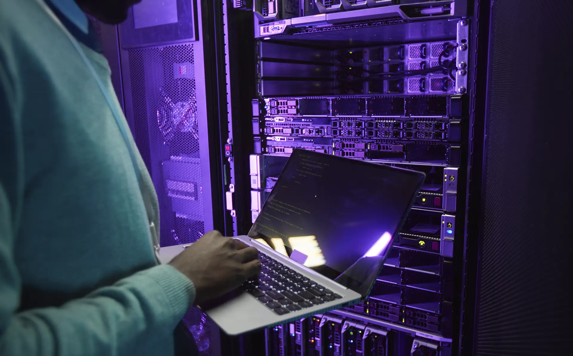 Engenheiro de dados segurando um laptop enquanto trabalha com um supercomputador em uma sala de servidores iluminada por luz azul. Representa a conexão entre tecnologia, performance de sites e segurança.